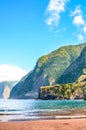 Amazing sand beach in Seixal, Madeira Island, Portugal. Green hills covered by tropical forests in the background. People swimming