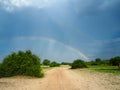 Amazing scene of natural sand route through green savanna plain with soft beautiful double rainbow on blue sky copy space