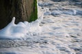 Amazing shot of sea waves hitting a stone column covered with moss and making splashes Royalty Free Stock Photo