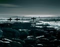 Amazing shot of the silhouettes of three surfers walking towards deep sea on a windy day