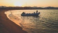 Amazing silhouette photo of inflatable boat with motor rocking on calm ocean waves at the sandy shore against sunset sky Royalty Free Stock Photo