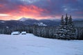 Amazing sunrise. Winter forest. Old wooden huts on the lawn covered with snow. High mountains with snow white peaks. Wallpaper Royalty Free Stock Photo