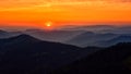 Amazing sunset over mountain range, scenic alpine landscape with dark silhouettes of mountains, fiery yellow sky and sun Royalty Free Stock Photo