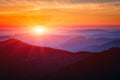 Amazing sunset over mountain range, scenic alpine landscape with dark silhouettes of mountains, fiery yellow sky and sun Royalty Free Stock Photo