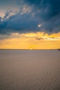 amazing vertical shot of the sun setting at the beach with footprints on sand and people on the horizon