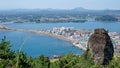 Amazing view of the city of the sea bay and mountain peaks on the horizon from a high volcano with a huge stone on the forefront o