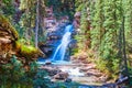 Amazing view of hidden waterfall at bottom of gorge with red rocks, moss sheets, and pine trees