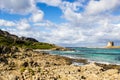 Amazing  view on the old aragonese tower in La Pelosa Beach. Beautifull rocks beach with green grass,  waves with foam and cloudly Royalty Free Stock Photo