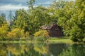 Amazing view of an old vintage wooden abandoned cabin, standing in woods reflected in lake calm water on sunny warm autumn day Royalty Free Stock Photo