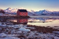 Amazing winter landscape with red rorbu, traditional scandinavian fishing house, snowy mountains in sunset light and blue sky Royalty Free Stock Photo