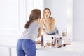 Amazing young woman doing her makeup in front of mirror. Portrait of beautiful girl near cosmetic table. Royalty Free Stock Photo