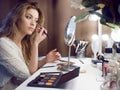 Amazing young woman doing her makeup in front of mirror. Portrait of beautiful girl near cosmetic table