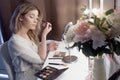 Amazing young woman doing her makeup in front of mirror. Portrait of beautiful girl near cosmetic table