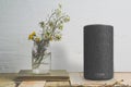 Amazon Alexa Echo plus next to a vase with some flowers on a wooden table against a white wall. Empty copy space