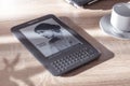 Amazon Kindle ebook reader on a wooden table next to a plant and a cup of coffee. Royalty Free Stock Photo