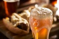 Amber beer with overflowing foamy head and bratwursts in background Royalty Free Stock Photo