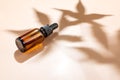 Amber bottle with cannabis oil used for medical purposes on beige background with daylight and the shadow of a hemp leaf