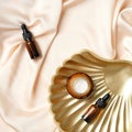 Amber glass cosmetic bottle, moisturizer cream and golden seashell on peach silk background Royalty Free Stock Photo