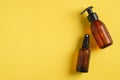 Amber glass cosmetic bottles in droplets of water. Refreshing beauty products on yellow background. Top view, flat lay