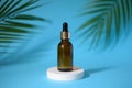 Amber glass dropper bottle with metallic lid on on the white podium with tropical leaves. Royalty Free Stock Photo