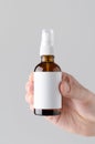 Amber Spray Bottle Mock-Up. Blank Label - Male hands holding an amber spray bottle on a gray background