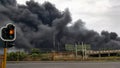 Traffic light in city with black toxic smoke in the background.