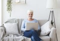 Ambitious senior lady using laptop on sofa at home