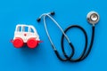 Ambulance service concept. Ambulance vehicle toy near stethoscope on blue background top view