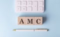 AMC word on wooden block with pen and calculator on blue background Royalty Free Stock Photo