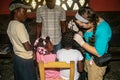 Amercan nurse examines patient in clinic as interpreter and mother look on.