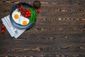 American breakfast with fried eggs, crispy bacon, cherry tomatoes and rocket salad served on the wooden table with knife and fork