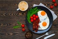 American breakfast with two fried eggs, crispy bacon, fresh cherry tomatoes, arugula and cup of cappuccino served on the wooden ta Royalty Free Stock Photo