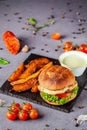 American burger with chicken cutlet, tomato, cucumber, green sauce. Sauce and for french fries on a black stone slate board Royalty Free Stock Photo