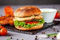 American burger with chicken cutlet, tomato, cucumber, green sauce. Sauce and for french fries on a black stone slate board Royalty Free Stock Photo