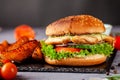 American burger with chicken cutlet, tomato, cucumber, green sauce. Sauce and for french fries on a black stone slate board Royalty Free Stock Photo