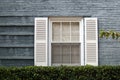 American casement window on the grey brick wall with green hedge