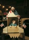 American cheerful family with usa flags play with rocket made out of cardboard box. Child cute boy play cosmonaut