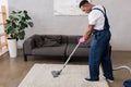 American cleaner in overalls and rubber glove cleaning carpet while working in living room Royalty Free Stock Photo