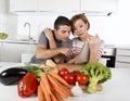 American couple in domestic kitchen wife following recipe in digital pad working together with husband