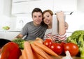 American couple in domestic kitchen wife following recipe in digital pad working together with husband