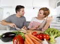 American couple in domestic kitchen wife following recipe in digital pad working together with husband