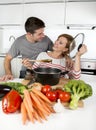 American couple at home kitchen smiling happy together wife cooking husband tasting the vegetable stew