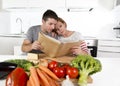 American couple working in domestic kitchen following recipe reading cookbook together