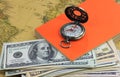 American dollars, vintage compass and orange book on background of old map Royalty Free Stock Photo