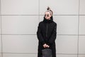 American fashionable young hipster woman in a long winter stylish black coat with a leather backpack with a bandana in sunglasses Royalty Free Stock Photo