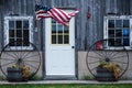 American Flag blowing in the wind by a door and two wagon wheels Royalty Free Stock Photo