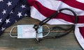 American flag with covid 19 Vaccination record card, personal facemask and stethoscope on fade blue rustic wood