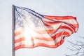 American flag flapping on sky with sunlight from back.