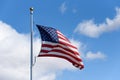 American flag flying in a breeze against a sunny blue sky with light white clouds Royalty Free Stock Photo