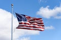 American flag flying in a breeze against a sunny blue sky with light white clouds Royalty Free Stock Photo